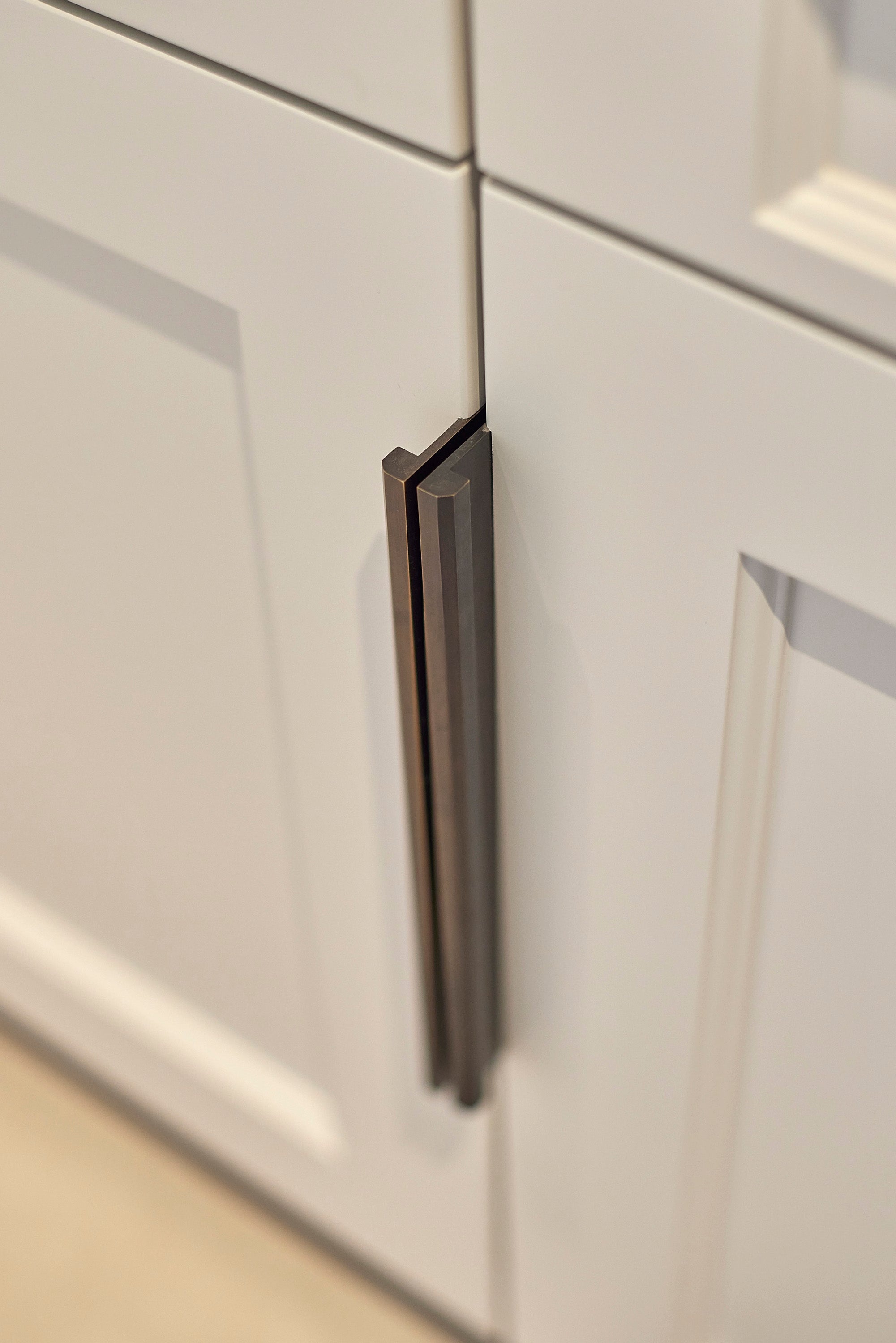 Close-up of a pair of dark bronze 'Arden' Edge pulls installed on the edges white cabinet door.