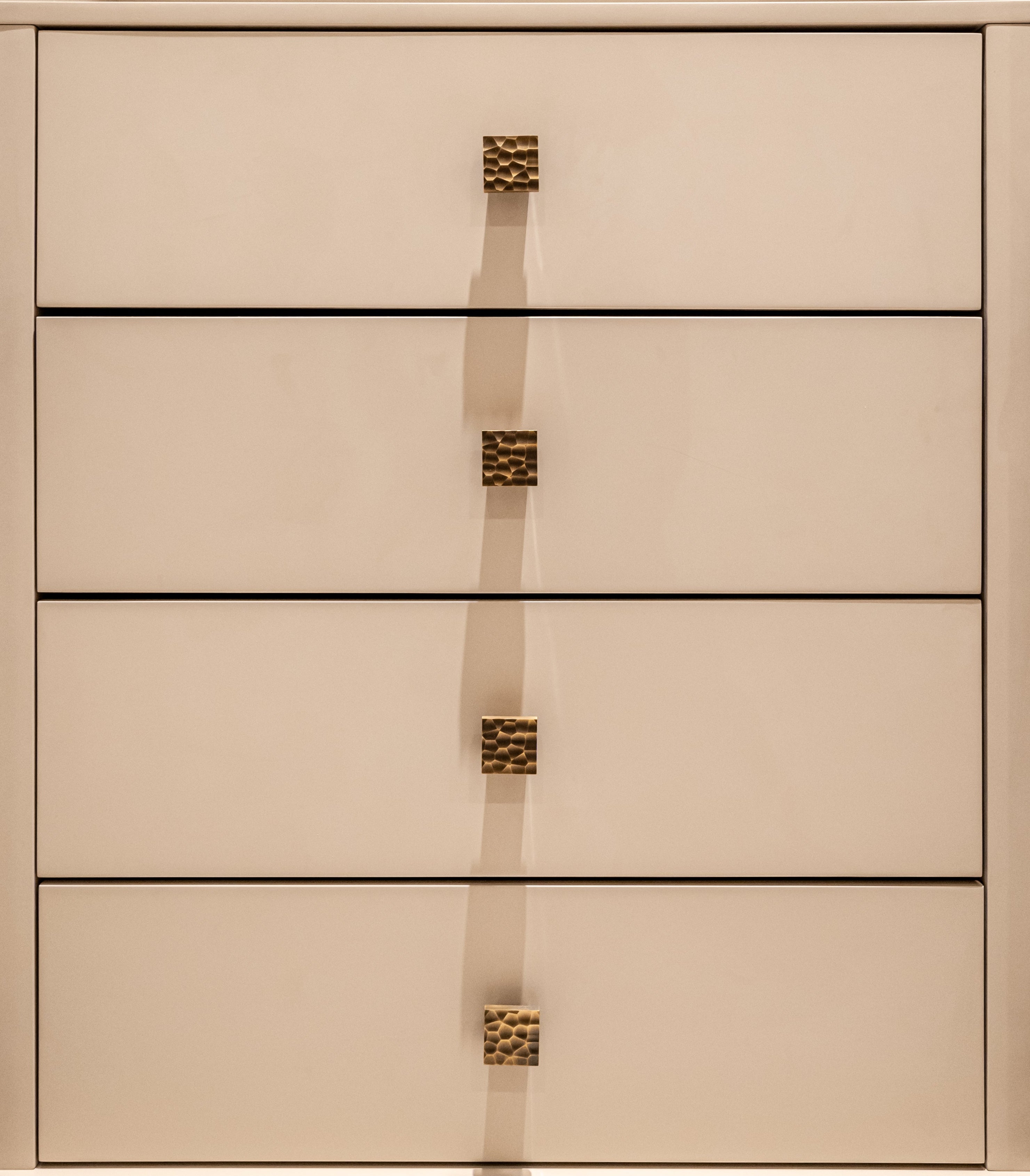 Beige dresser draws with antique brass hammered 'lapworth' cabinet knobs installed on each drawer front.