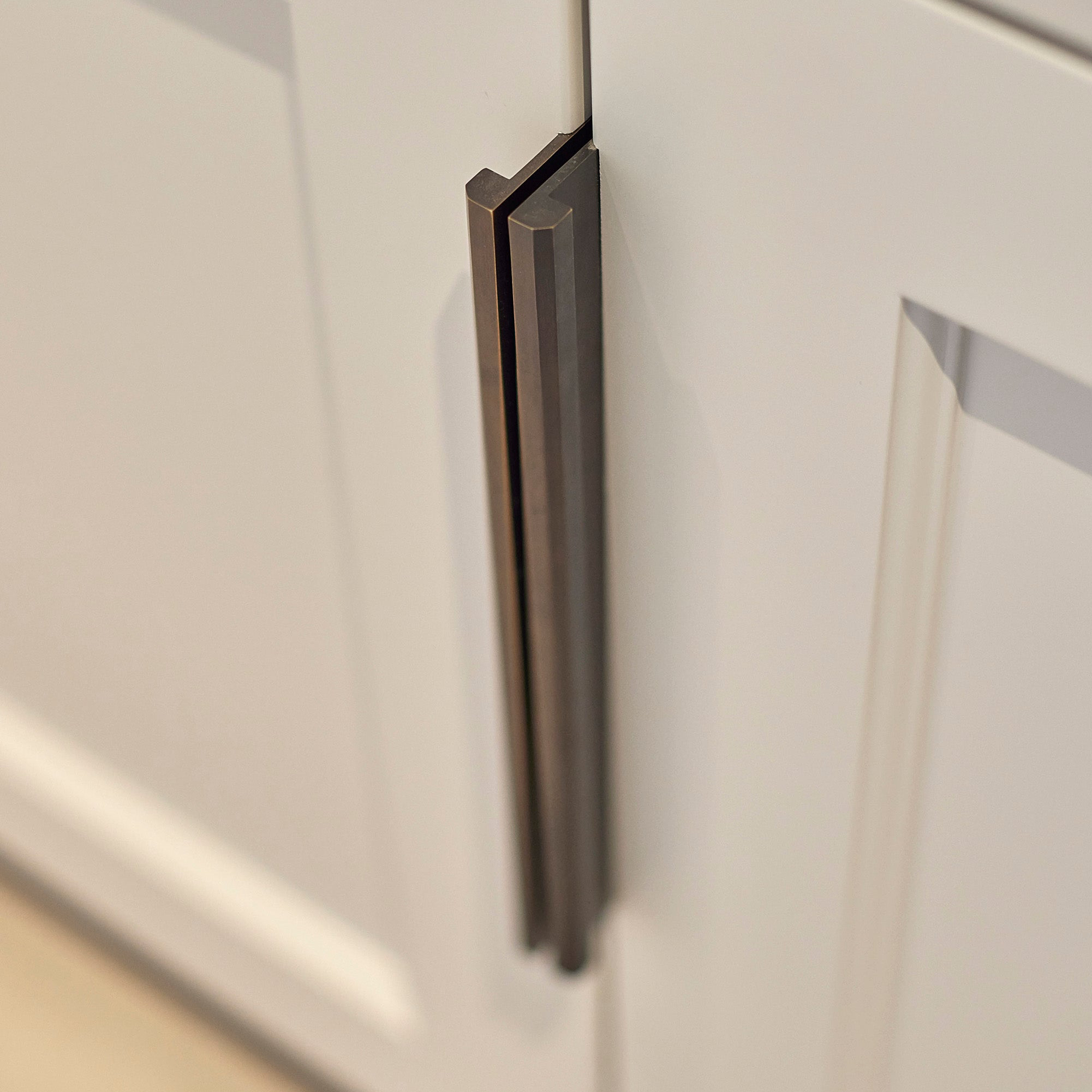 Close-up of a dark bronze edge pull on a white cabinet door