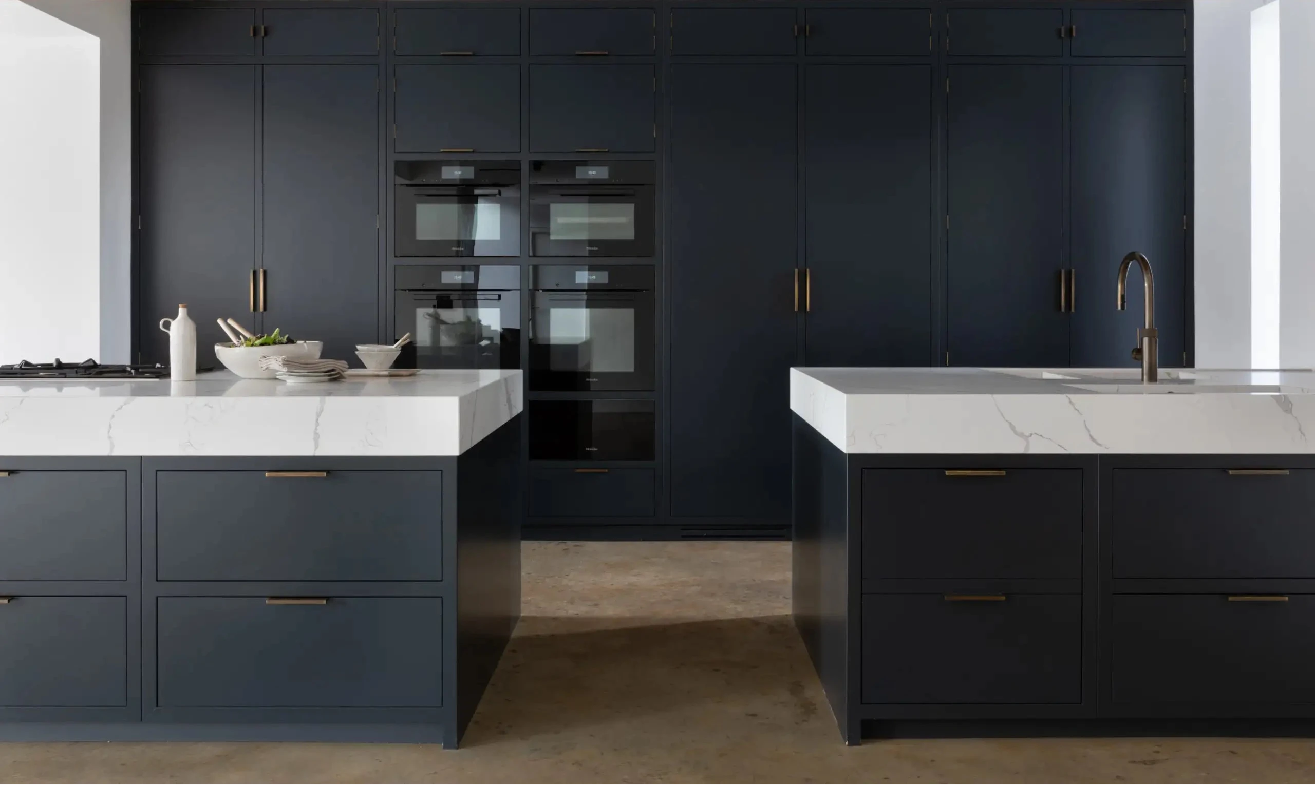 Modern kitchen with dark blue cabinets and white countertops with Antique Brass 'Knowle' Edge Pull Handle install on each cabinet and door.