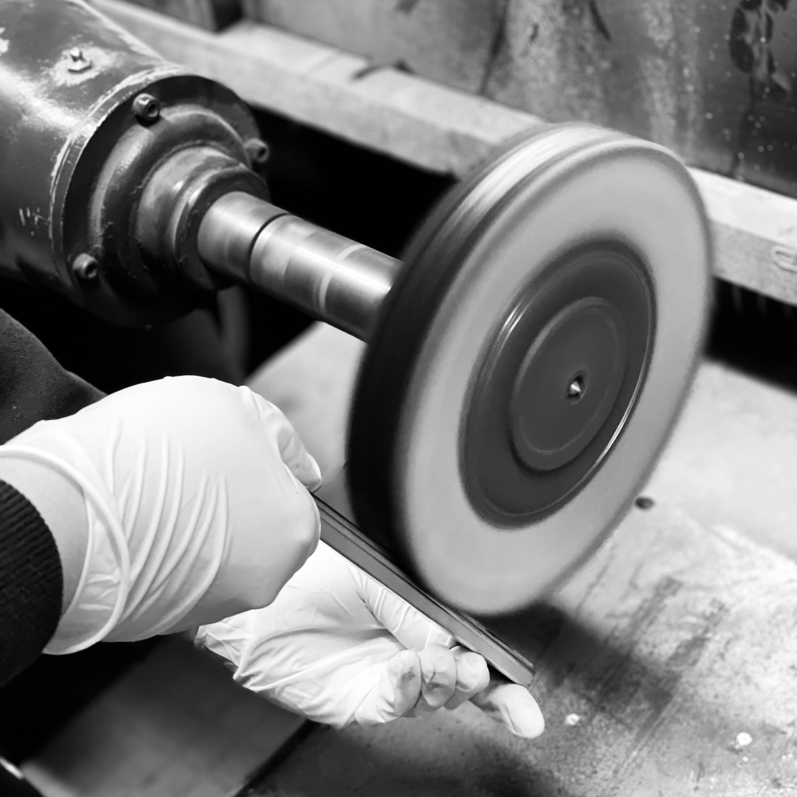 Close up black and white image of a cabinet pull being hand-polished on a polishing lathe.